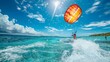 © Prostock-studio - A person is parasailing in the ocean on a sunny day, with the parachute billowing above them as they are pulled by a boat.