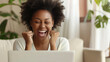 © CosmoJulia - Excited Black Woman Celebrating Success on Laptop at Home