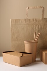 Wall Mural - Eco friendly food packaging. Paper containers, bag and straws on white table against beige background