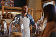 © peopleimages.com - Bakery, happy and man in cafe with customer for serving pastry, cakes and baked foods for small business. Restaurant, coffee shop and waiter or barista by counter for service, help and talk to woman