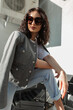 Cool beautiful fashion curly girl with stylish sunglasses in fashionable clothes with a trendy jacket and jeans posing on the street