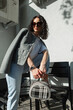 Fashion beautiful curly lady with sunglasses in fashionable casual clothes with blazer and jeans with handbag posing on the street with sun rays