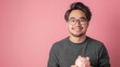 Asian man in casual attire holding a pink piggy bank in front of a vibrant pink wall.