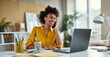 © BrightSpace - A woman is sitting at a desk with a laptop and a cell phone. She is smiling and talking on the phone,wearing yellow clothes
