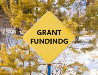 Grant funding symbol. Concept words Grant funding on beautiful yellow road sign. Beautiful forest snow blue sky background. Business and grant funding concept. Copy space.