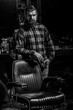 © Yevhen - Portrait of a barber sitting in a barber's chair in his workplace. Man barber in shirt standing near chair in grooming salon. Black and white