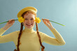 Fashionable happy smiling redhead freckled woman wearing yellow beret, ribbed turtleneck,  holding daffodils, posing on blue background. Close up studio portrait. Copy, empty, blank space for text