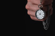 Man holding chain with elegant pocket watch on black background, closeup. Space for text