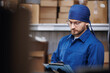 Young worker in blue uniform use clipboard checklist for manage parcel box product in warehouse. Online service of logistic import export concept