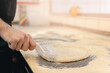 Pizzamaker stretches dough, worker removes air with roller from fresh food pizza, top view. Business pizzeria concept