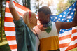Affectionate multiracial couple in love with American flag in nature.