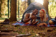 Happy couple of campers using cell phone while relaxing in nature.