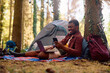 Happy black man using cell phone and laptop while camping in nature.