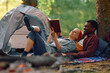 Relaxed couple reading book while camping in forest.