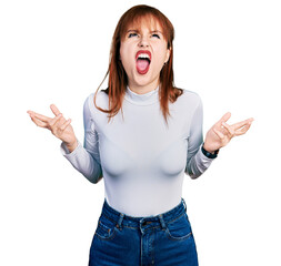 Wall Mural - Redhead young woman wearing casual turtleneck sweater crazy and mad shouting and yelling with aggressive expression and arms raised. frustration concept.