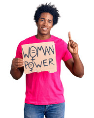 Sticker - Handsome african american man with afro hair holding woman power banner surprised with an idea or question pointing finger with happy face, number one