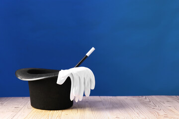 Wall Mural - Magician's hat, wand and gloves on wooden table against blue background, space for text