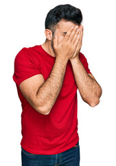 Wall Mural - Hispanic man with beard wearing casual red t shirt with sad expression covering face with hands while crying. depression concept.