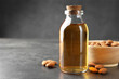 Almond oil in bottle, bowl and nuts on grey textured table, closeup. Space for text
