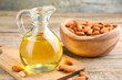 Almond oil in jug and nuts on wooden table, closeup