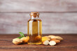 Almond oil in bottle, nuts and leaves on wooden table, closeup