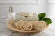 Loofah sponges, soap, towels and green leaves on white marble table