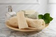 Loofah sponges, soap, towel and green leaves on white marble table