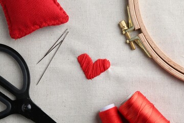 Wall Mural - Embroidered red heart, needles, hoop and scissors on light cloth, top view