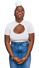 Wall Mural - Young african woman with turban wearing hair turban over isolated background smiling and laughing hard out loud because funny crazy joke with hands on body.