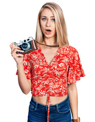 Sticker - Beautiful young blonde woman holding vintage camera scared and amazed with open mouth for surprise, disbelief face