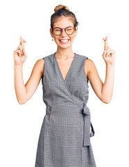 Beautiful caucasian woman with blonde hair wearing business clothes and glasses gesturing finger crossed smiling with hope and eyes closed. luck and superstitious concept.