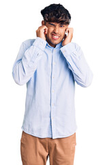 Sticker - Young hispanic man wearing casual shirt covering ears with fingers with annoyed expression for the noise of loud music. deaf concept.