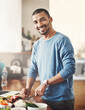 © peopleimages.com - Cooking, meal and man with knife for vegetables, food and dinner in home. Vegan, diet and healthy eating with portrait and recipe for nutrition, smile and male person in kitchen with ingredients