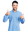 © Krakenimages.com - Hispanic man with beard wearing casual business shirt success sign doing positive gesture with hand, thumbs up smiling and happy. cheerful expression and winner gesture.