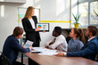 © artiemedvedev - Female leader presents colorful pie chart on tablet to colleagues during office meeting. Attentive team engages in strategic planning, analysis, empowerment workplace.