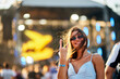 © artiemedvedev - Smiling young woman enjoys summer music festival, beach stage backdrop, makes peace sign, sunlit hair, casual fashion, vibrant nightlife scene. Audience, live concert, fun, youth, dance vibe.