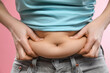 © New Africa - Woman touching belly fat on pink background, closeup. Overweight problem