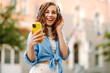 © maxbelchenko - Young woman dancing and listening music with headphones and smart phone in the street. Street style. Beauty and fashion.