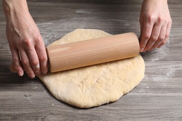 Woman rolling raw dough at wooden table, closeup