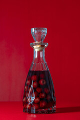 Wall Mural - Homemade cherry brandy in glass bottle on a red background, closeup