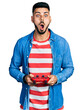 © Krakenimages.com - Young hispanic man with beard playing video game holding controller afraid and shocked with surprise and amazed expression, fear and excited face.