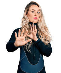 Poster - Young blonde woman wearing diver neoprene uniform moving away hands palms showing refusal and denial with afraid and disgusting expression. stop and forbidden.