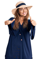 Poster - Middle age hispanic woman wearing summer hat approving doing positive gesture with hand, thumbs up smiling and happy for success. winner gesture.