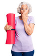 © Krakenimages.com - Senior grey-haired woman holding yoga mat covering mouth with hand, shocked and afraid for mistake. surprised expression