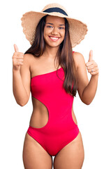 Poster - Young beautiful latin girl wearing swimwear and summer hat success sign doing positive gesture with hand, thumbs up smiling and happy. cheerful expression and winner gesture.