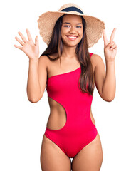 Canvas Print - Young beautiful latin girl wearing swimwear and summer hat showing and pointing up with fingers number seven while smiling confident and happy.