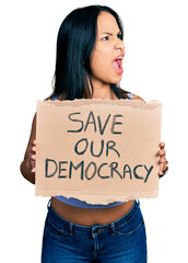 Wall Mural - Beautiful hispanic woman holding save our democracy protest banner angry and mad screaming frustrated and furious, shouting with anger. rage and aggressive concept.