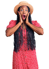 Wall Mural - Young african american woman wearing summer hat afraid and shocked, surprise and amazed expression with hands on face