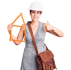 Sticker - Young beautiful woman wearing architect hardhat holding build project smiling happy and positive, thumb up doing excellent and approval sign