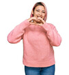 © Krakenimages.com - Hispanic woman with pink hair wearing casual winter sweater smiling in love doing heart symbol shape with hands. romantic concept.